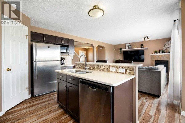 Kitchen with island, stainless steel appliances, and view into living room with fireplace and television. - 459 Citadel Meadow Bay Nw, Calgary