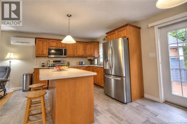 Kitchen with natural wood cabinets, stainless steel refrigerator, and island with bar stools. - 459 Saint-ignace, Saint Louis De Kent