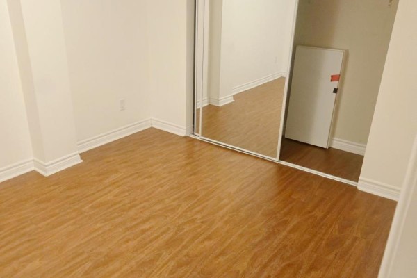 Corner of a room with wood laminate flooring and a large mirrored closet reflecting the opposite wall. - 4594 Bismark Crescent, Mississauga