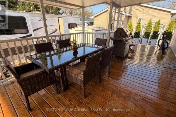 Covered wooden deck with a glass-top dining table, chairs, and a barbecue. - 46 - 497 County Rd 36 Road, Trent Lakes