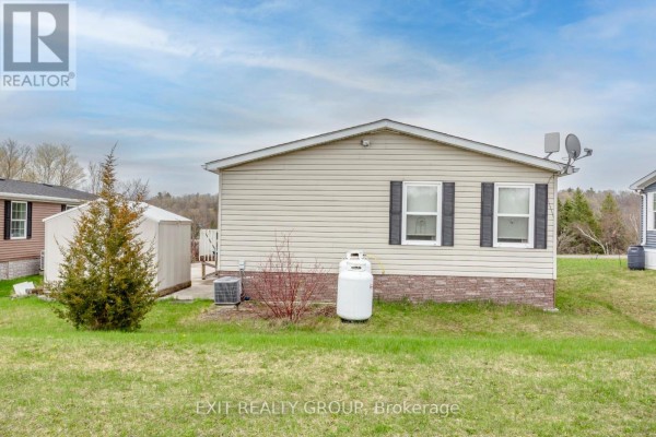 Rear side of a beige mobile home with two windows, a storage shed, and propane tanks. - 46-152 Concession Road 11 W, Trent Hills