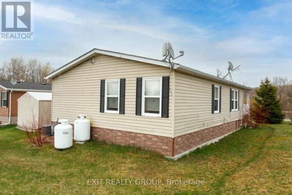 Angled view of the beige mobile home's rear and side, showing windows and propane tanks. - 46-152 Concession Road 11 W, Trent Hills