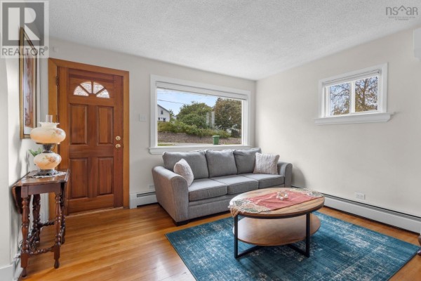 Living room with wood door, sofa, coffee table, blue rug, hardwood floors, and large window. - 46 Adelaide Avenue, Halifax