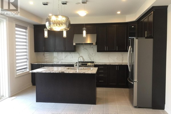 Modern kitchen with dark brown cabinets, granite countertops, and a large island with pendant lights. - 46 Blazing Star Street, East Gwillimbury