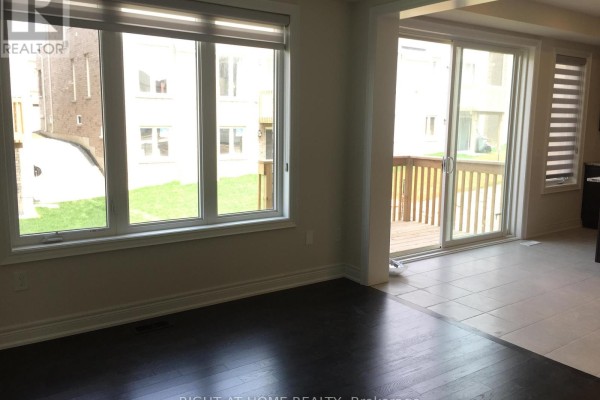 Living room area with dark hardwood floors and large windows overlooking a backyard deck and neighboring houses. - 46 Blazing Star Street, East Gwillimbury