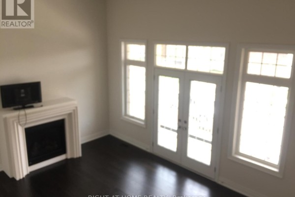 Living room with dark hardwood floors, a white fireplace, and French doors with tall windows. - 46 Blazing Star Street, East Gwillimbury