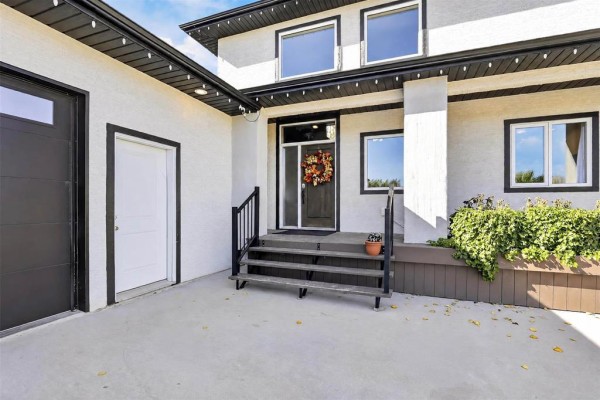 Close-up of the house entrance with a white door, black garage door, and steps leading to the front door. - 46 Carleton Drive, Steinbach