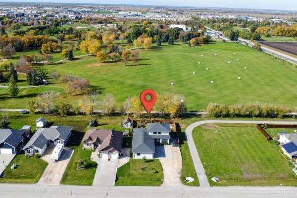 Aerial view of the house and property with a golf course in the background and a red location pin. - 46 Carleton Drive, Steinbach