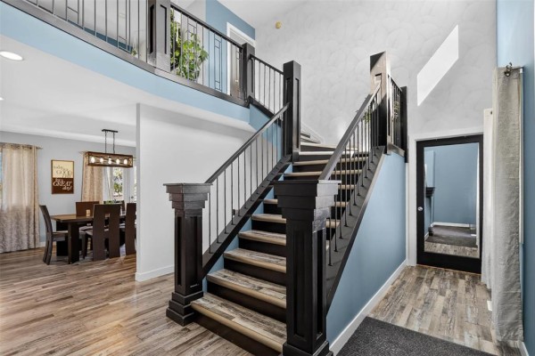 Interior view of a staircase with dark wood railings, light blue walls, and a view of a dining room. - 46 Carleton Drive, Steinbach