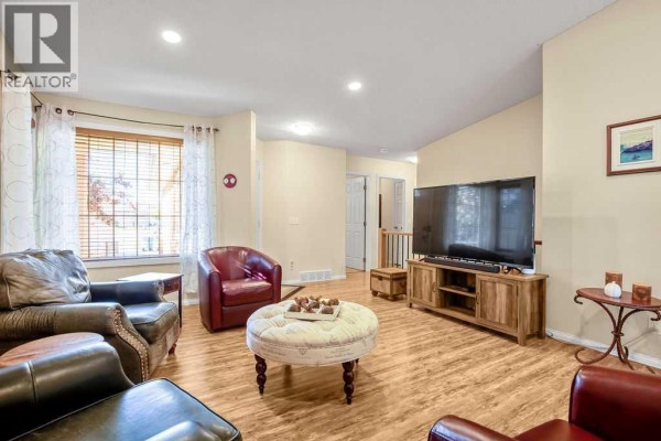 Living room with leather chairs, a round ottoman, wood-look flooring, and a large television. - 46 Harvest Grove Green Ne, Calgary