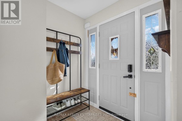 Interior entryway with a light grey door, coat rack with jackets and bags, and a bench with shoes. - 46 Marilyn Crescent, Halton Hills
