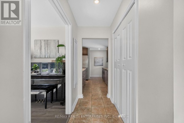 Hallway view looking towards a living room with a piano and into the kitchen. Features tiled flooring and double doors. - 46 Marilyn Crescent, Halton Hills