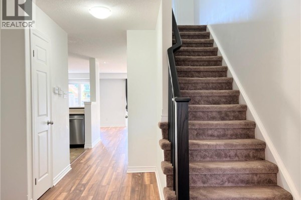 Hallway with wood-look flooring, a staircase with brown carpet, and doorways. - 46 Renfrew Street, Kitchener