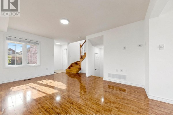 Bright living room with large windows, polished wood floors, and a staircase with black railings. - 46 Ridwell Street, Barrie