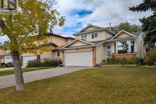 Side view of a two-story house with yellow siding, brick accents, and a double garage. - 460 Hawkhill Place Nw, Calgary