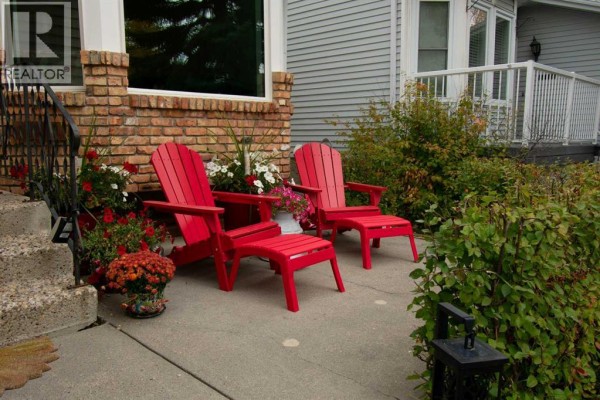 Two red Adirondack chairs and ottomans on a paved patio with potted flowers. - 460 Hawkhill Place Nw, Calgary
