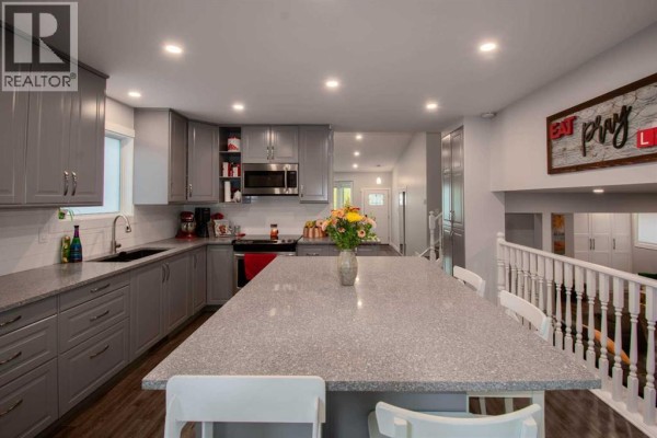 Modern gray kitchen with a large granite island, stainless steel appliances, and pendant lighting. - 460 Hawkhill Place Nw, Calgary