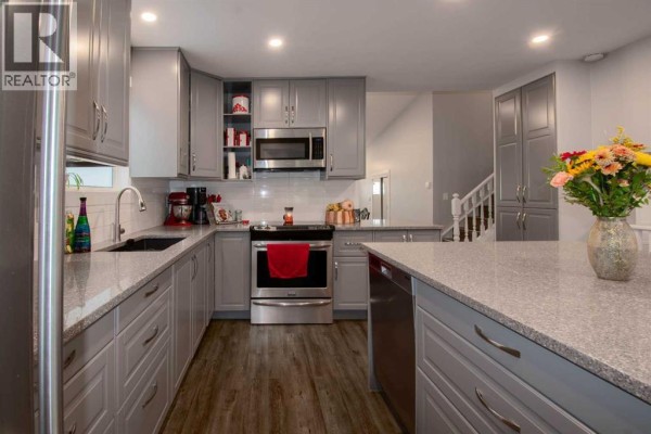 U-shaped gray kitchen with granite countertops, stainless steel appliances, and a kitchen island. - 460 Hawkhill Place Nw, Calgary
