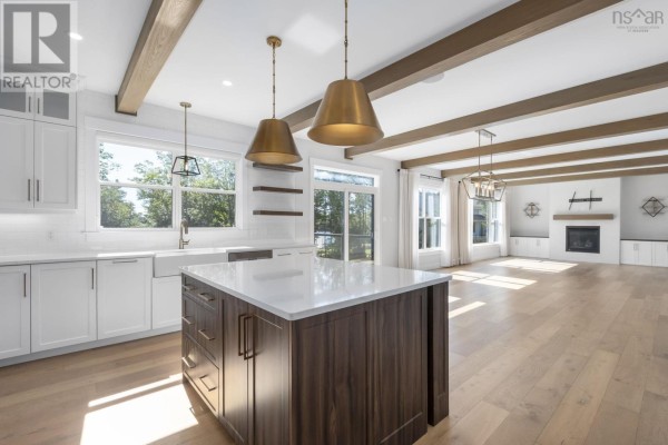 Modern kitchen with white cabinets, a large island, and an open concept living area with a fireplace. - 460 Mccabe Lake Drive, Middle Sackville