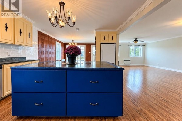 View from the kitchen island towards a living area with wood-look flooring and white walls. - 460 Vanier Street, Campbellton