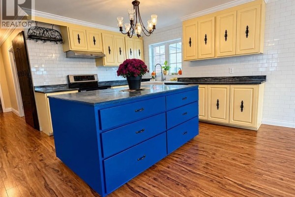 Kitchen featuring yellow cabinets, white subway tile backsplash, stainless steel appliances, and a blue island. - 460 Vanier Street, Campbellton