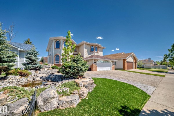 Exterior view of a beige house with a landscaped rock garden and pond, a paved driveway, and blue sky. - 4608 43 Av Nw, Edmonton