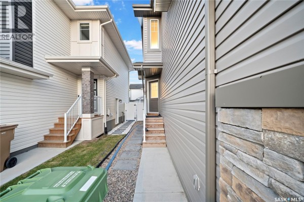 View of the narrow side yard between two attached townhouses with grey siding. - 4608 Mutrie Crescent, Regina