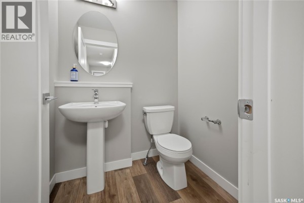 Half bathroom with a white pedestal sink, toilet, and an oval mirror on the wall. - 4608 Mutrie Crescent, Regina