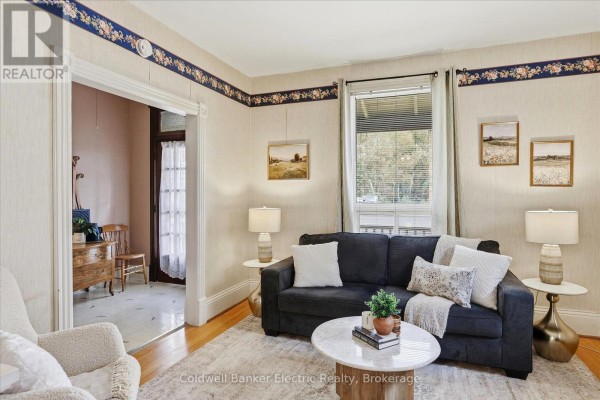 Living room with a charcoal sofa, white accent pillows, and floral wallpaper. - 461 Murray Street, Peterborough