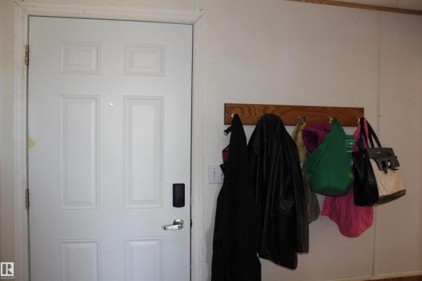 White front door with a black handle and coats hanging on a wooden rack. - 4610 51 Av, Myrnam