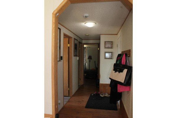 Hallway with wood laminate flooring, coat rack, and doors leading to rooms. - 4610 51 Av, Myrnam