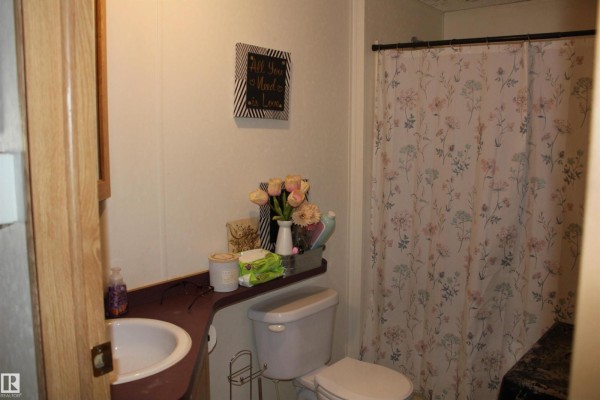Bathroom with a pink sink, white toilet, and a floral shower curtain. - 4610 51 Av, Myrnam