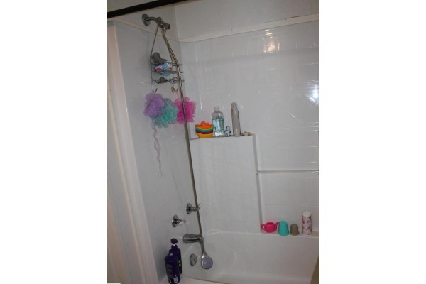 White bathtub with a showerhead, caddy, and bath accessories. - 4610 51 Av, Myrnam