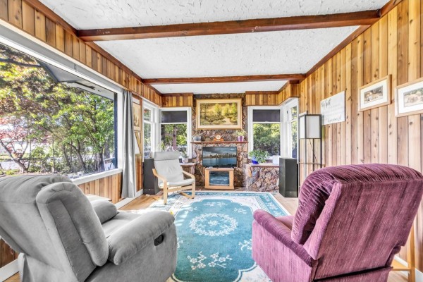 Living room with wood-paneled walls, large windows, stone fireplace, and two recliners. - 46133 Third Avenue, Chilliwack Proper East, Chilliwack