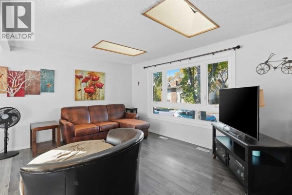 Living room with a brown leather sectional sofa, large window, and television. - 4615 31 Avenue Ne, Calgary
