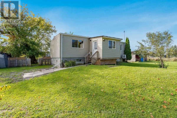Rear exterior of the house showing beige siding, grass, and trees. - 4617 Concession Road 2 Sunnidale, Clearview