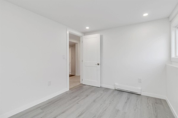 White room with light grey wood-look flooring, a white closet, and a doorway to a tiled hallway. - 46190 Larch Avenue, Chilliwack Proper South, Chilliwack