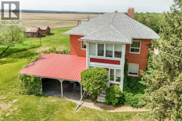 Aerial view of red brick farmhouse with sunroom and covered patio, surrounded by greenery. - 46218 Rr 203, Rural Camrose County