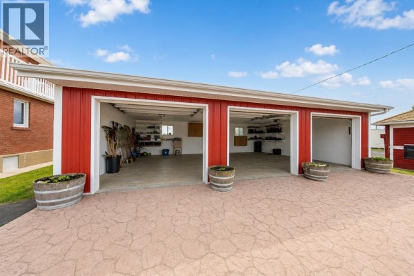 Three-bay garage with red exterior and white trim, concrete driveway, and planters. - 46218 Rr 203, Rural Camrose County