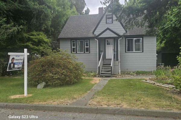 Exterior of a grey two-story house with a peaked roof and a for sale sign in the front yard. - 46240 Gore Avenue, Chilliwack Proper East, Chilliwack