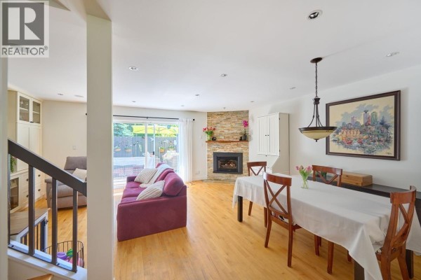 Living and dining area with a fireplace, hardwood floors, and white walls. - 4627 Hoskins Road, North Vancouver