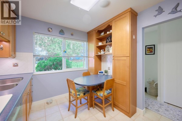 Dining area with a table set for four, a corner fireplace, and a view into the kitchen. - 4627 Hoskins Road, North Vancouver