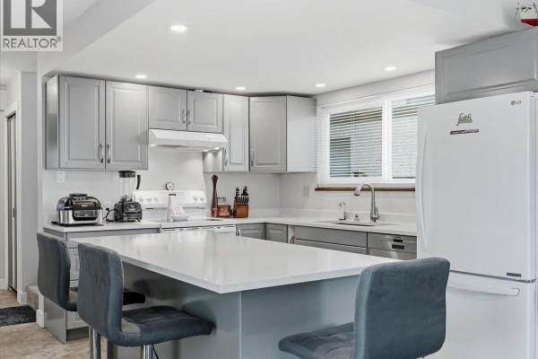 Another view of the kitchen island, white countertops, grey cabinets, and stainless steel sink and dishwasher. - 4628 Hermitage Drive, Richmond