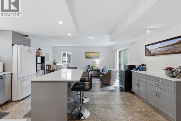 Open concept living area showing a kitchen island, seating area with wicker furniture, and a dining table. - 4628 Hermitage Drive, Richmond
