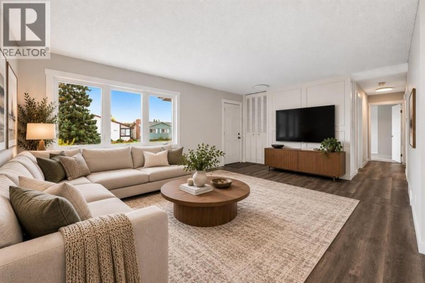 Living room with a large sectional sofa, wood coffee table, and entertainment unit. - 4628 Marcombe Road Ne, Calgary