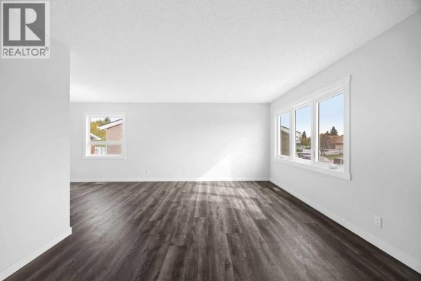 Spacious empty room with large windows and dark wood-look flooring. - 4628 Marcombe Road Ne, Calgary