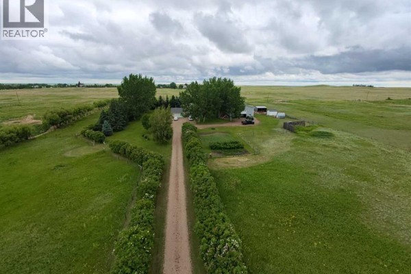 Aerial view of a rural property featuring a house, garage, evergreen trees, and open fields under a bright sky. - 463, 181043 Hwy 550, Rural Newell, County Of
