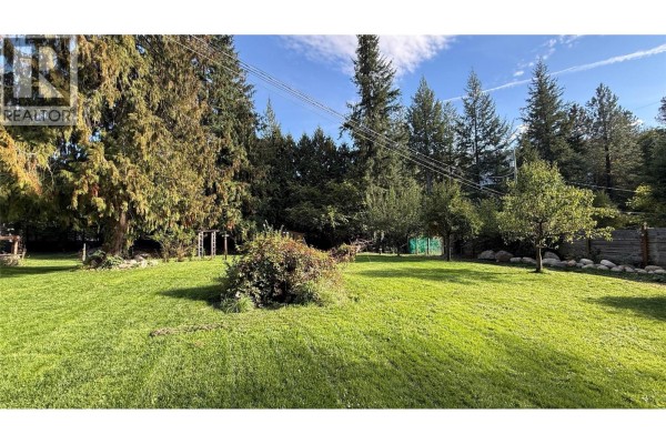 Expansive lawn with scattered trees and shrubs, a wooden fence, and a backdrop of tall evergreens. - 4630 3a Highway, Nelson