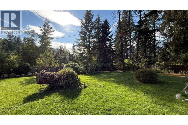 Sunny backyard with green grass, surrounded by tall trees and natural landscaping elements. - 4630 3a Highway, Nelson