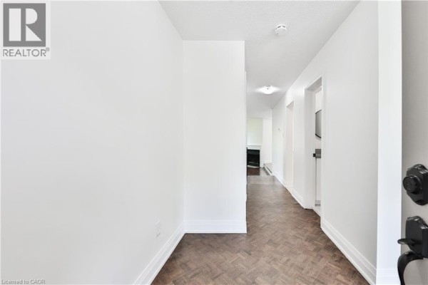 Interior hallway with white walls and dark parquet flooring leading to doorways. - 4635 Regents Terrace Unit# 2, Mississauga